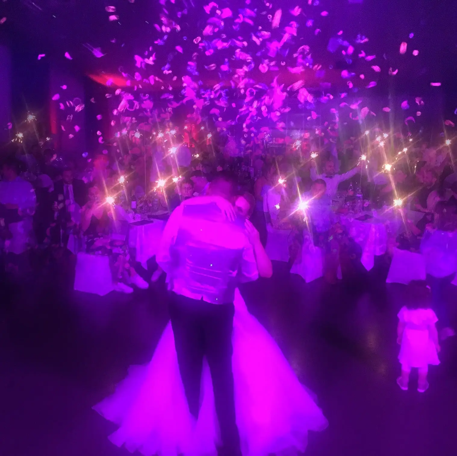 Mariés dansant sous des confettis et une lumière violette